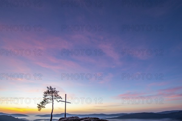 Summit cross on a sandstone rock in the middle of the forest. Landscape with a marvellous view over a misty forest. Sunrise in the Palatinate Forest, Germany, Europe