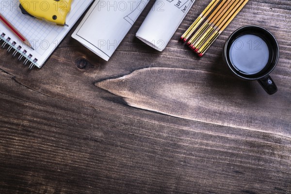 Checked copybook pencil blueprints measuring tape wooden meter and cup of coffee on pine wood board