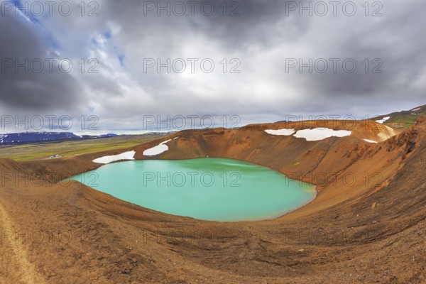 Lake water bright green color. On the shores lie snowfields from last year. Picturesque lake in the crater of an extinct volcano