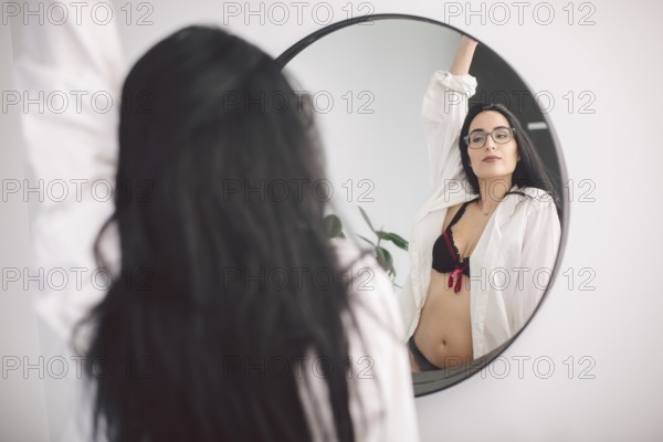 Beautiful young woman in underwear looking at mirror in morning at home. Young woman looking herself reflection in mirror at home. Beauty and people concept. Good morning. Morning makeup
