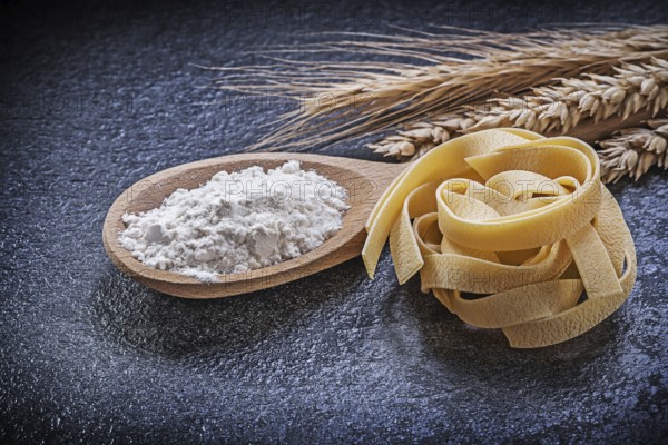 Wheat rye ears wooden spoon flour pasta on black background