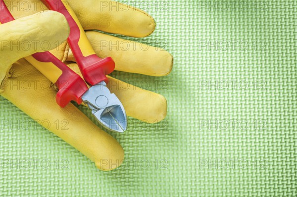 Yellow protective gloves sharp nippers on green background electricity concept