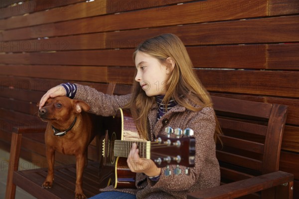 Blond kid girl playing guitar with dog and winter beret on wooden background