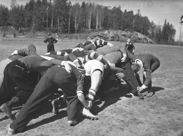 1940s rugby. A group of rugby players are practising on a sunny spring day. The focus is on the ball and all players try their best to get their hands on it. Sweden May 2 1940. Kristoffersson ref 128-12