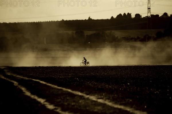 A cyclist rides through the atomised haze of a tractor