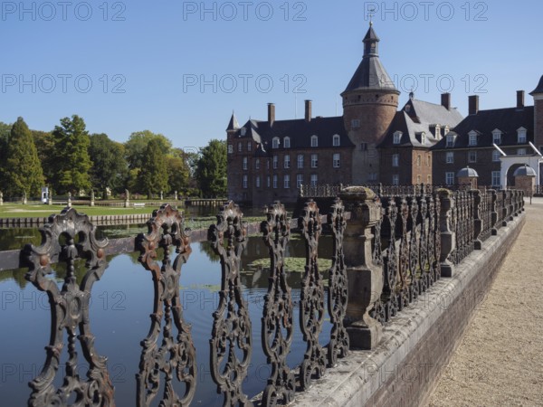 Ornate iron fence along a moat with a view of a brick castle, anholt, isselburg, münsterland, germany