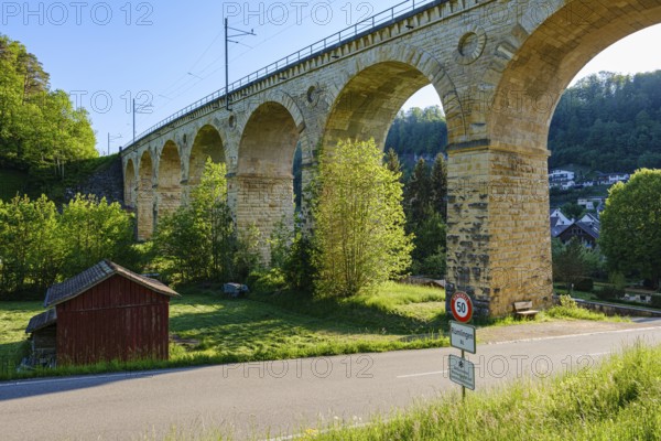 A massive stone viaduct towers over a green landscape with a small country road in the foreground, Rümlingen, Basel-Landschaft, Switzerland, Europe