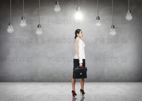 Business woman stands in a gray room with hanging bulbs