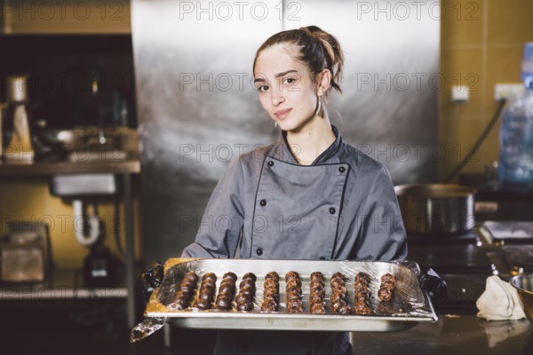 Subject profession and cooking pastry. young Caucasian woman with tattoo of pastry chef in kitchen of restaurant preparing round chocolate candies handmade truffle in black gloves and uniform