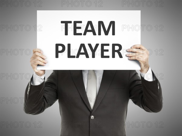 A business man holding a paper in front of his face with the text team player