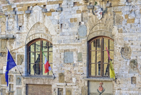 Windows, flags and a coat of arms on the facade of Palazzo Nuovo del Podesta in San Gimignano, Italy, Europe