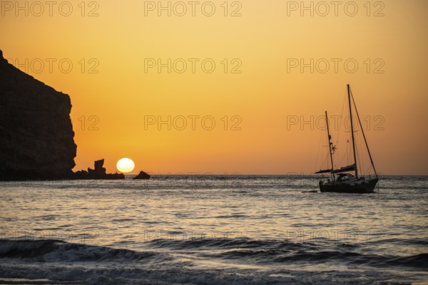 Sunrise during a storm, Calima. A haze-covered horizon turns orange as the sun rises as a ball. A boat is anchored in the sea. Landscape photograph in Gran Tarajal, Canary Islands, Spain, Europe