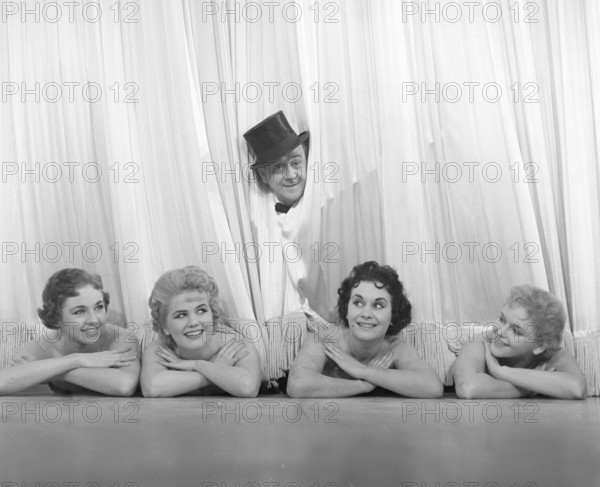 Fun in the 1950s. A gentleman and four ballet dancers at the theatre. He's wearing a top hat when peeping out from the stage curtain. He is actor Åke Söderblom, 1910-1965. Sweden 1955. Photo Kristoffersson Ref BR116-11