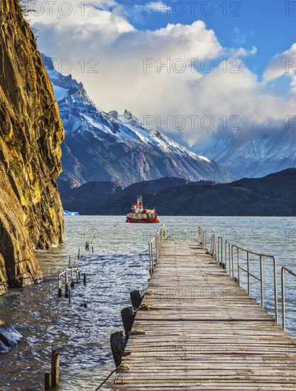 Pleasure boat for tourists swim with wooden pier. Grey Lake in the national park Torres del Paine, Chile, South America