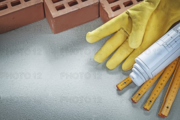 Red bricks safety gloves blueprints wooden meter on concrete background building concept
