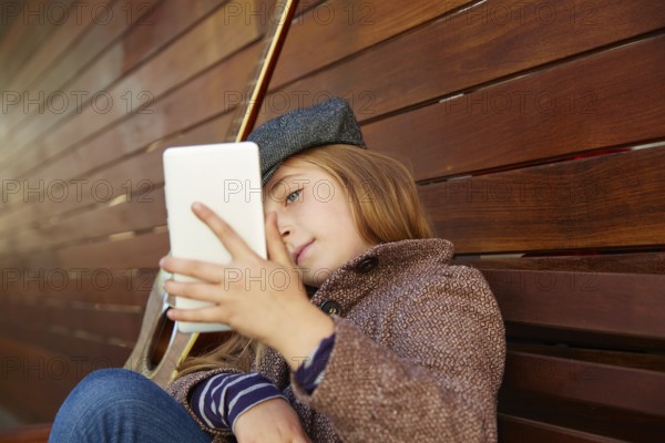 Blond kid girl taking selfie with guitar and winter beret and coat on wooden background