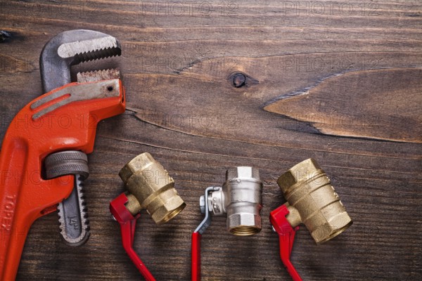 Plumbers fixtures with red handles and monkey wrench on vintage wooden board with copyspace construction concept
