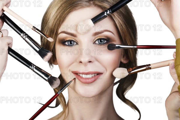 Many hands with cosmetics brushes doing make-up to glamour woman, over white background