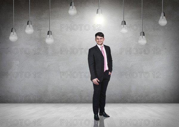 Businessman stands in a gray room with hanging bulbs
