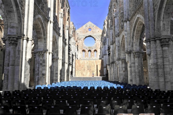 Church ruins of the Cistercian Abbey of San Galgano, Abbazia San Galgano, Gothic, Chiusdino, Tuscany, Italy, Europe, Interior of a ruined church with rows of chairs facing forwards, open stone arches and blue sky above, Europe