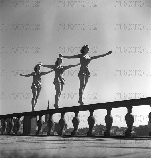 Gymnastics in the 1950s. Three young female gymnasts are standing on the wall outside Stockholm city hall. The three hold their arms legs and body in the same position. Sweden Photo Kristoffersson ref CZ67-9