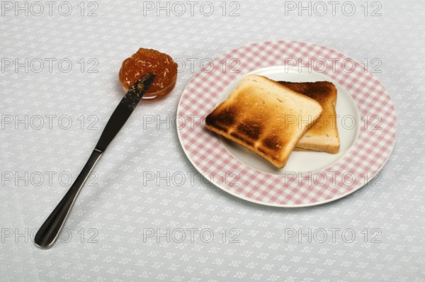 Slice of bread spread with jam and knife on a small bowl