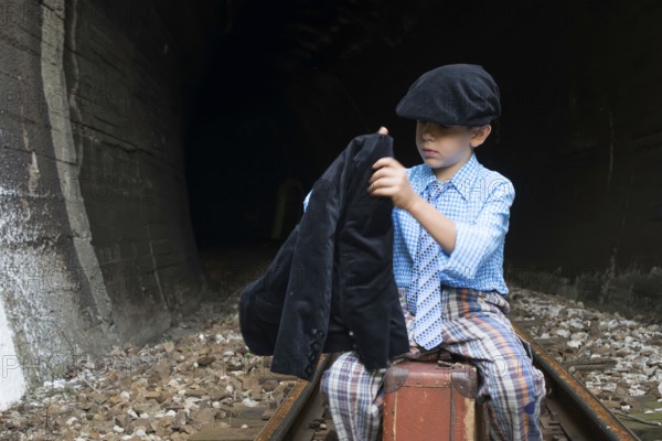 Child in vintage clothes sits on railway road in front of a tunnel