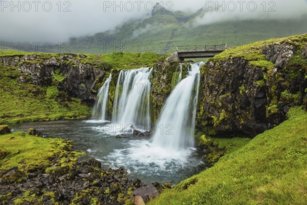 Threaded full-flowing waterfall on the grassy mountains. Iceland - country of mountains, rivers and waterfalls