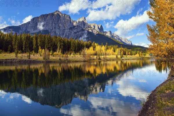 Outskirts of Canmore. Lush autumn in the Canadian Rockies. Cumulus clouds reflected in the smooth water of the lake. The concept of active, ecological and photo tourism
