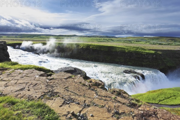 Iceland. Grand Gullfoss. In mid-July, bubbling water illuminated by a bright morning sun