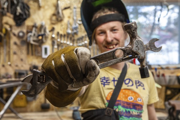 A front portrait view of a skilled tradesman showing his handmade multi-tool, consisting of a hammer, spanner and ratchet wrench welded together