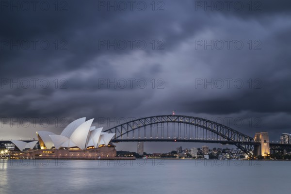 SYDNEY, AUSTRALIA, DECEMBER 03 2023: Sydney Opera House and Harbour Bridge at dusk during a summer storm from Mrs Macquarie's Chair in Sydney, New South Wales, Australia, Oceania
