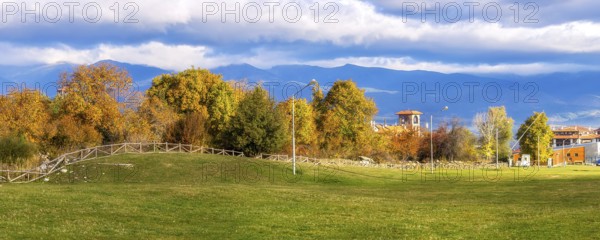 Bansko, Bulgaria autumn panorama banner background with colorful green, red and yellow trees, Rila mountains and house tower