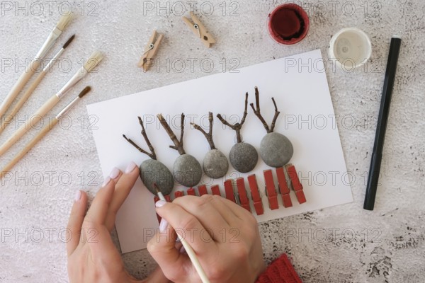 Diy Merry Christmas deer on greeting card postcard made of pebbles, sea stones, clothespins and branches on white background. Natural Eco style diy. Gift idea. Step by step. Top view. Process kid children craft. Do it yourself