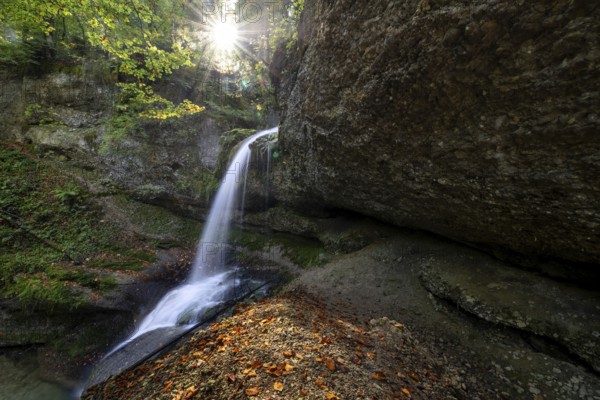 A waterfall flows over mossy rocks, illuminated by sunbeams breaking through the leaves, Hasenreuter Wasserfall, Scheidegg, Bavaria, Germany, Europe