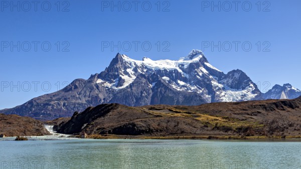 Snowy mountain above a calm river and turquoise water under a blue sky, The landscape of the Torres del Paine National Park in Patagonia in Chile