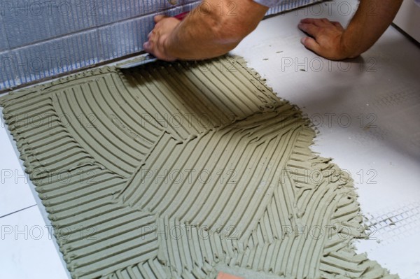 A tiler at work. Gluing floor tiles with tile adhesive and trowel. Austria
