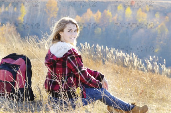 Young happy woman having fun outdoors sitting on the top of the hill. Backpacking tourism concept