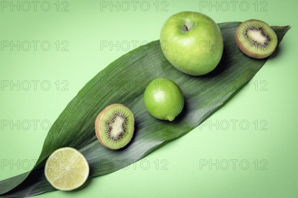 Mix of raw fruits on a green leave. Green kitchen table with fresh detox fruits