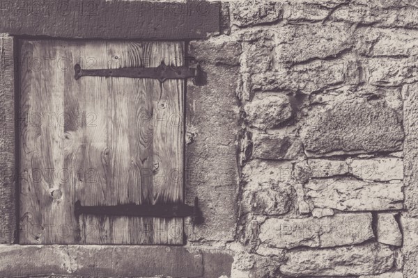 Architectural frame with a weathered wooden trap door and the stone wall, from a traditional german house
