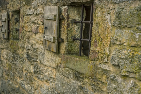 Medieval stone wall with two small windows, fortified with metal bars