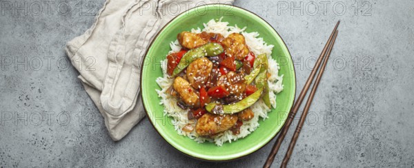 Asian sweet and sour sticky chicken with vegetables stir-fry and rice in ceramic bowl with chopsticks top view on gray rustic stone background, traditional Asian dish, food photography, food photography