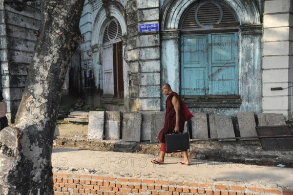 07.10.2013, Yangon, Myanmar, Asia, A Buddhist monk walks with his briefcase past an old colonial building on the famous Strand Road, Asia