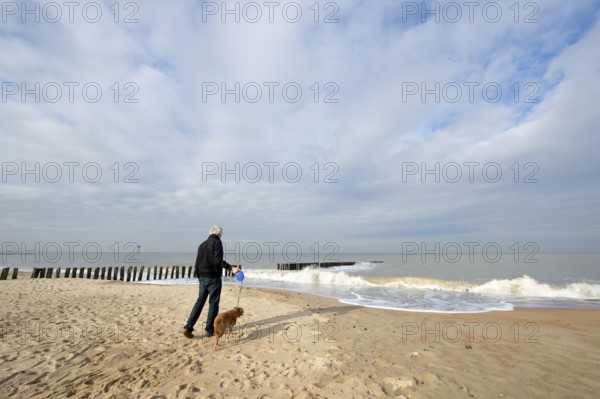 Man with dog at the beach in Dutch Zeeland
