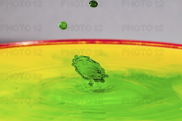 A green drop hits a yellow-green liquid and creates colourful patterns, water droplets, collision, high-speed photography, concept, water figures