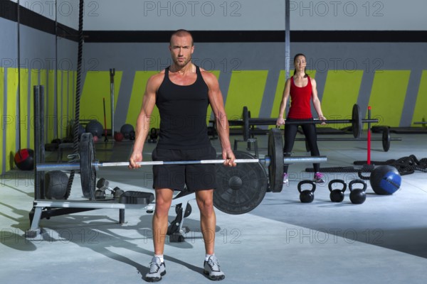 Gym man and woman with weight lifting bar workout in crossfit exercise