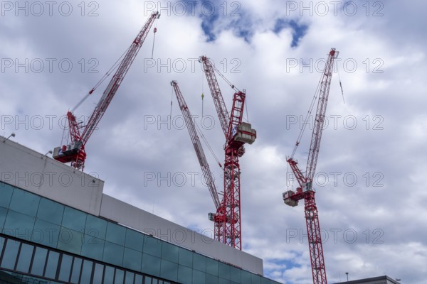 Several red construction cranes in front of a building complex under a cloudy sky, Berlin, Germany, Europe