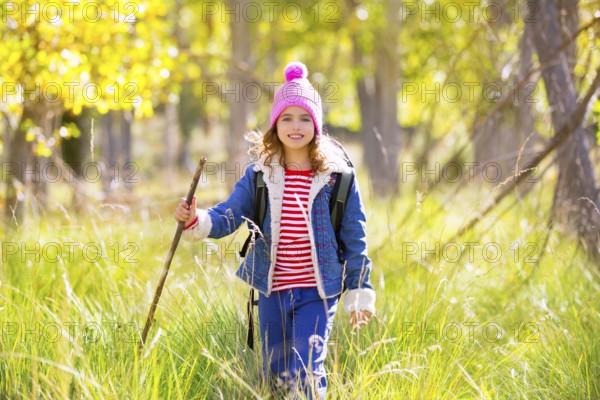 Hiking kid girl with backpack in autum poplar trees forest and walking stick