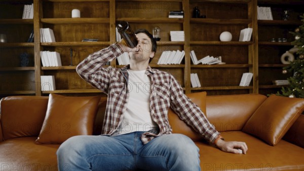 Alcohol addiction at young age. Caucasian male cannot stop drinking alcohol, drunken lonely male drinks wine from bottle. Loneliness, depression and alcoholism during Christmas and New Year holidays
