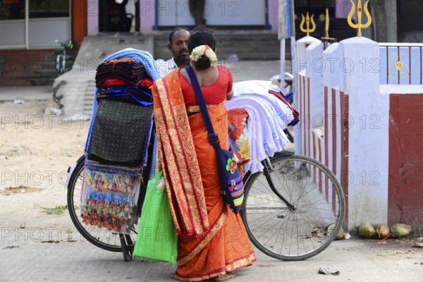 Kanchipuram, Tamil Nadu, South India, A traditionally dressed woman carries colourful fabrics on a bicycle through the street, Kanchipuram, Tamil Nadu, South India, India, Asia